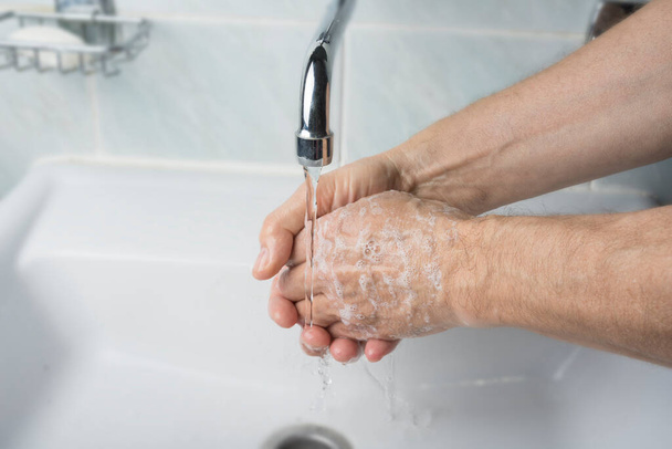 Older male is washing his hand under faucet - Фото, зображення