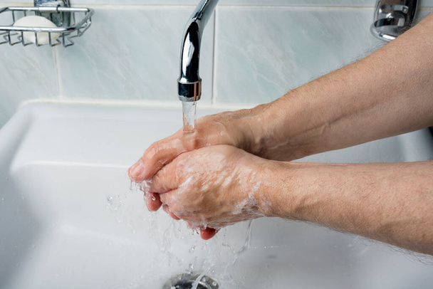 Hombre mayor se lava la mano bajo el grifo
 - Foto, imagen