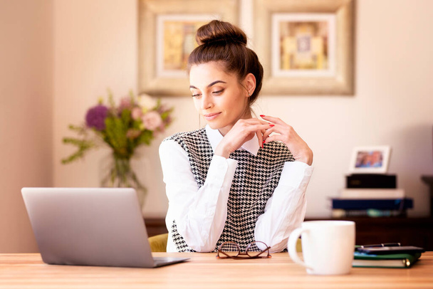 Lövés vonzó fiatal nő néz figyelmes, miközben ül a laptop mögött, és dolgozik otthonról.  - Fotó, kép