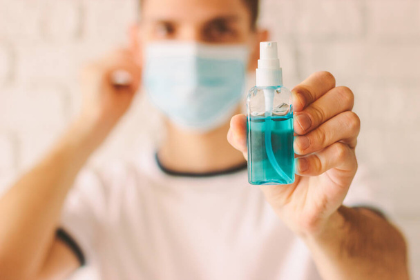 Confident man presenting and showing bottle of antibacterial gel in hand. Young doctor wearing medical mask on face and holding sanitizer in hand. Preventive measures against coronavirus COVID-19 - Φωτογραφία, εικόνα