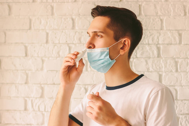 Portrait of young sick man using nasal drops for runny congested nose. Confident sick doctor in medical protective mask on face using nose spray. Pandemic coronavirus COVID-19 nCov-19 symptoms - Foto, Imagen