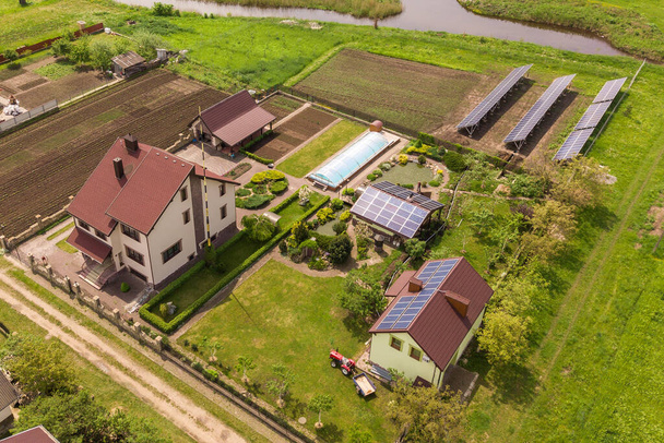 Luftaufnahme eines Privathauses im Sommer mit blauen Photovoltaik-Solarzellen auf dem Dach und im Hof. - Foto, Bild