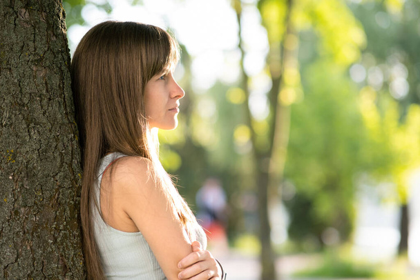 Hübsche junge Frau mit langen Haaren steht im Sommer ordentlich im Baumstamm. - Foto, Bild
