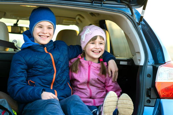 Zwei glückliche Kinder sitzen zusammen im Kofferraum eines Autos. Fröhlich umarmen sich Bruder und Schwester im Kofferraum des Familienfahrzeugs. Wochenendreisen und Urlaubskonzept. - Foto, Bild