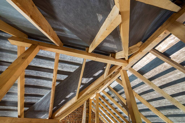 Dachgeschoss eines im Bau befindlichen Gebäudes mit Holzbalken einer Dachkonstruktion und Ziegelwänden. - Foto, Bild