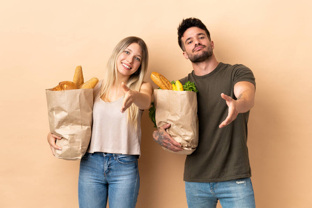Пара держащих сумки с продуктами на изолированном фоне пожимающих руки для закрытия хорошей сделки
 - Фото, изображение