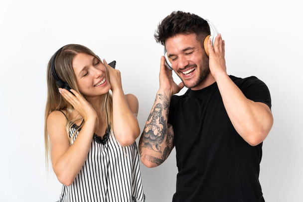 Young caucasian couple on white background listening music - Foto, afbeelding