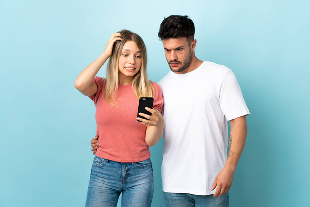 Giovane coppia caucasica isolata su sfondo blu che legge un messaggio con il cellulare - Foto, immagini