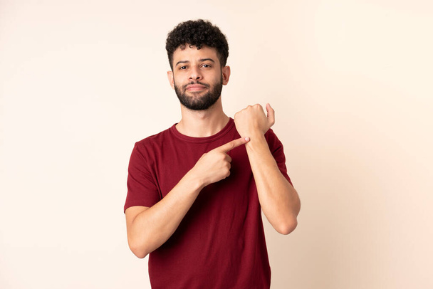 Young Moroccan man isolated on beige background making the gesture of being late - Photo, Image