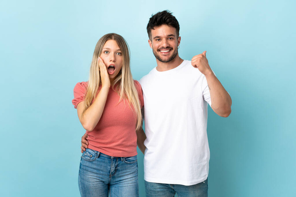 Young caucasian couple isolated on blue background pointing finger to the side and presenting a product - Foto, Imagem