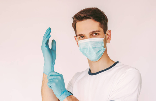 Portret szczęśliwy chirurg w masce ochronnej umieścić na medycznych rękawic lateksowych izolowane białe tło. Młody, pewny siebie lekarz w masce medycznej nosi rękawiczki ochronne. Ochrona COVID-19 - Zdjęcie, obraz