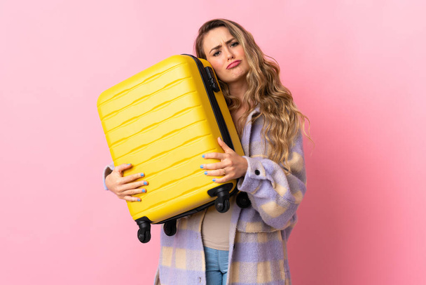 Young Brazilian woman isolated on pink background in vacation with travel suitcase and unhappy - Фото, изображение