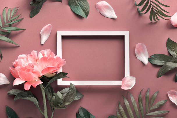 Creative flat lay with light coral peony and exotic palm leaves around white empty blank frame with copy-space on rosy brown or dark beige background. - Fotó, kép
