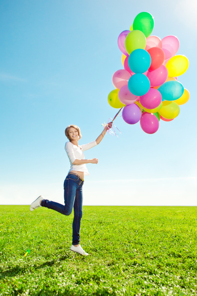 Young woman with balloons in hands in the field against the sky - Foto, Imagen