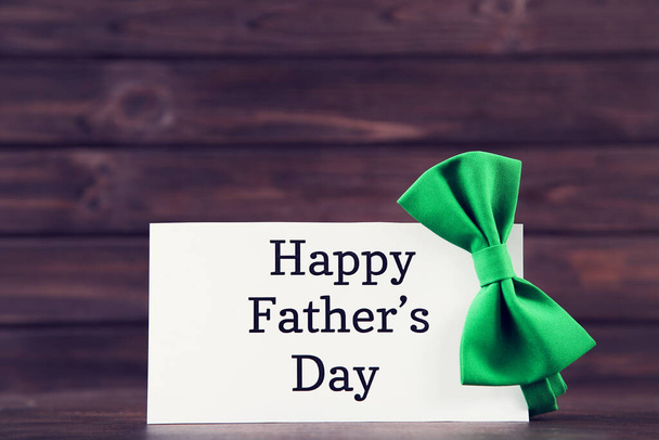 Text Happy Father's Day with green bow tie on brown wooden table - Foto, imagen