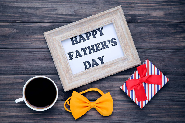 Text Happy Father's Day with cup of coffee, gift box and bow tie on wooden table - Photo, image