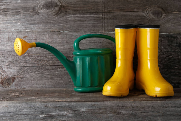 Yellow rubber boots and  garden watering can on vintage wooden background with  copy space. - Photo, image