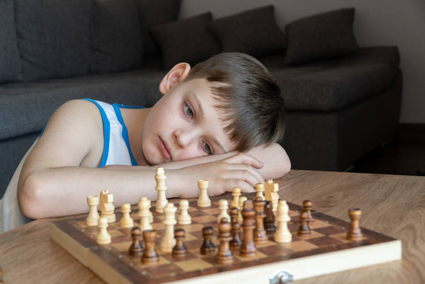 The serious child lost in thought playing chess. Playing board games, on coronavirus quarantine. The child playing chess. - Photo, Image