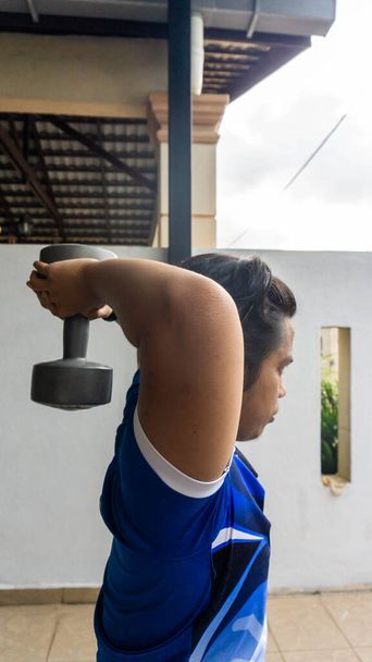 Un joven atlético levantando pesas y haciendo ejercicio en casa. Fitness, deporte y estilo de vida saludable. Enfoque selectivo en primer plano
. - Foto, Imagen