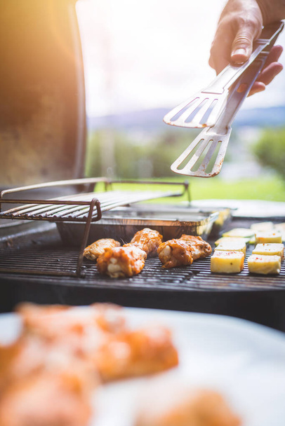 Close up of chicken wings, cheese and vegetables on gas grill. Summer time, outdoors. - Fotó, kép