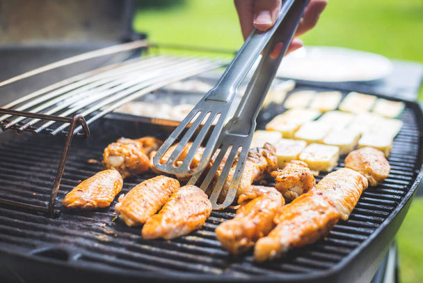 Close up of chicken wings, cheese and vegetables on gas grill. Summer time, outdoors. - Фото, изображение