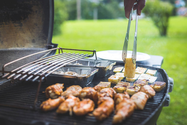 Close up of chicken wings, cheese and vegetables on gas grill. Summer time, outdoors. - 写真・画像