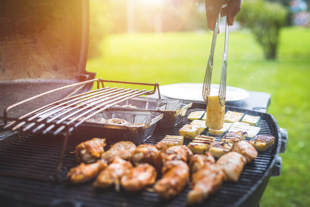 Close up of chicken wings, cheese and vegetables on gas grill. Summer time, outdoors. - Photo, image