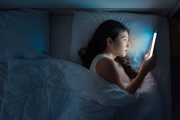 Femme regardant la télévision ou le contenu multimédia dans une tablette sur le lit dans la nuit - Photo, image