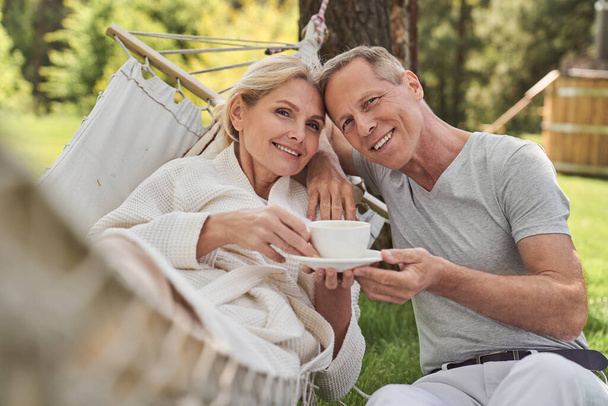 Happy spouses drinking tea from one cup outdoors - Foto, immagini