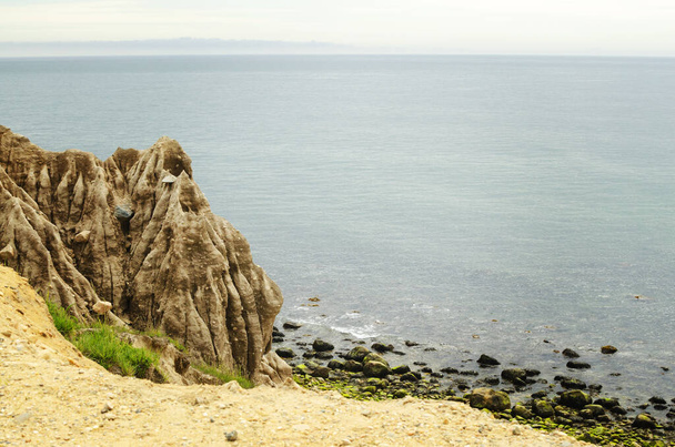 Края обрыва глины после дождя эрозин на широкой открытой пустой береговой линии океана с мхом пород
 - Фото, изображение