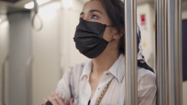 Mujer joven asiática usa máscara protectora negra, mirando la tabla horaria de la estación en el tren del metro, nuevo estilo de vida de distancia social normal, autoprotección, coche de metro vacío, precaución de riesgo infeccioso MOCIÓN LENTA - Imágenes, Vídeo
