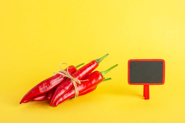 Red hot chili pepper and a small blackboard on a yellow background. - Фото, зображення