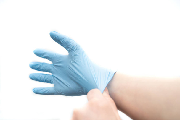 het aantrekken van een wegwerp latex handschoen op een witte achtergrond - Foto, afbeelding