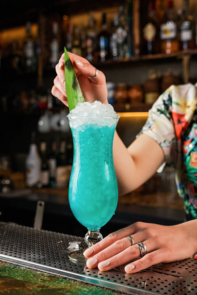 Lady bartenger garnishing blue hawaii cocktail with a banana leaf - Foto, Imagem