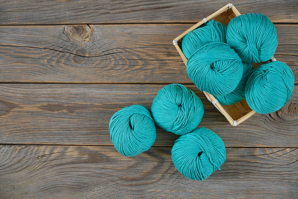 Цветные шарики пряжи для вязания лежат в плетеной корзине на деревянном фоне
. - Фото, изображение