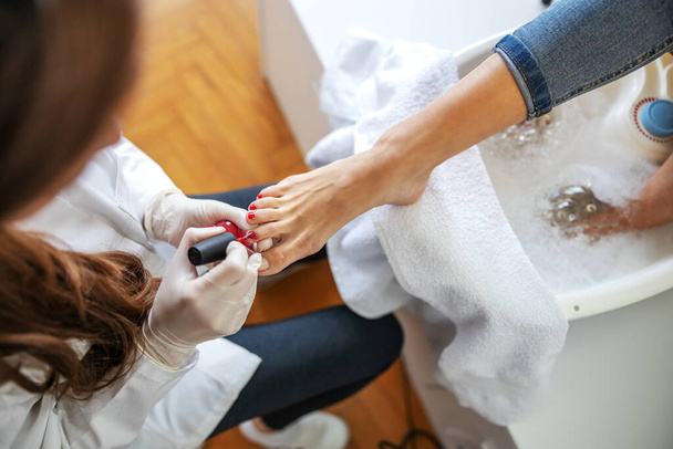 Top view of beautician putting nail polish on toes. Beauty salon interior. - Фото, изображение