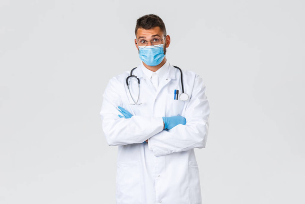 Covid-19, egészségügyi dolgozók, világjárvány és a vírus terjedésének megelőzése. Meglepett spanyol férfi orvos orvosi maszkban és köpenyben felemeli a szemöldökét csodálkozva, érdekes eseteket hall a klinikán. - Fotó, kép
