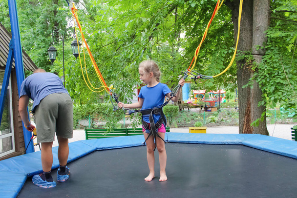 La fille heureuse souriante sautant avec bungee dans le trampoline au parc contre les arbres verts - Photo, image