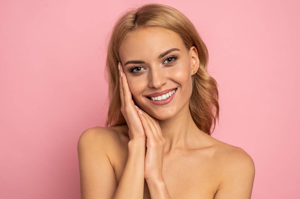 Image of adorable half-naked woman smiling at camera and touching her face isolated over pink background. - Photo, Image