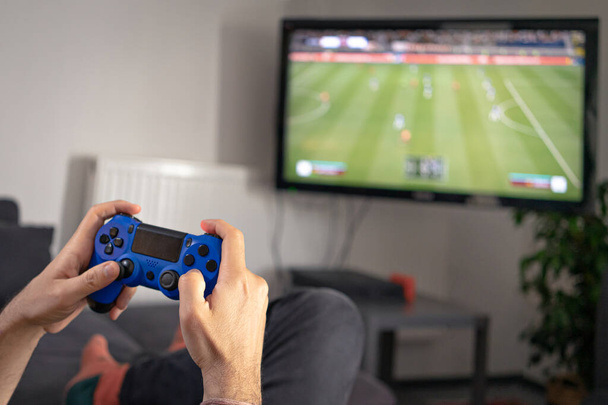 рука людини тримає джойстик і грає в відеоігри вдома на тренерському дивані перед телевізором з ігровою консоллю
 - Фото, зображення
