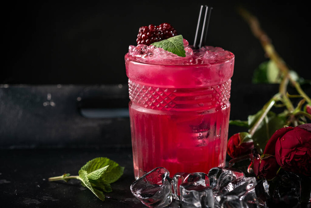 Alkoholinen cocktail karhunvatukoilla, mintulla ja jäällä tummalla puupohjalla. Virkistävä punainen juoma lasissa - Valokuva, kuva
