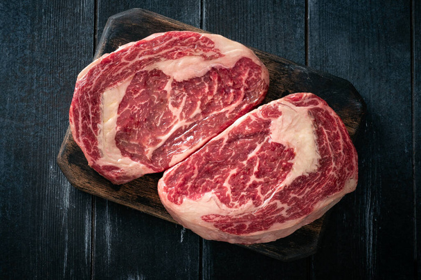Perfect raw rib eye beef steak on black wooden background, top view - Foto, Bild