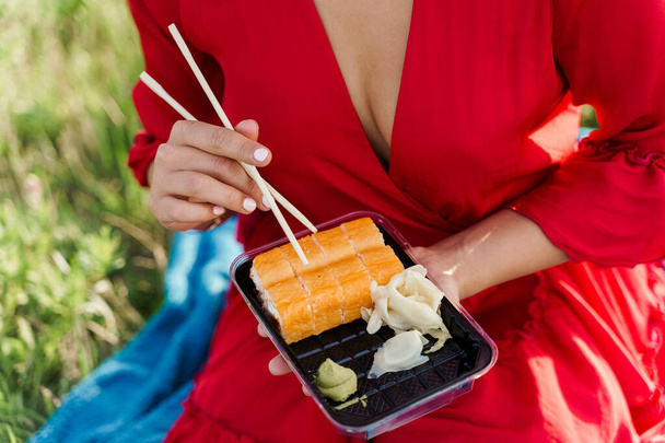 Sushi-Set in Großaufnahme. Attraktives Mädchen hält Sushi mit Essstäbchen in den Händen. Kurier lieferte Sushi-Set für hübsche Frau. Black Box mit Sushi, Wasabi, Ingwer. - Foto, Bild