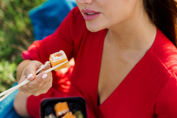 Detailní souprava sushi se dotýká rtů. Atraktivní dívka drží sushi s hůlkami v rukou. Kurýr doručil sushi set pro hezkou ženu. Černá krabice se sushi, wasabi, zázvorem. - Fotografie, Obrázek