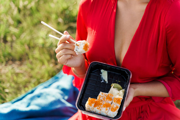 Nahaufnahme Sushi-Set Essensausgabe. Sexy girl hält Sushi mit Essstäbchen in der Hand. Kurier lieferte Sushi-Set für hübsche Frau. Black Box mit Sushi, Wasabi, Ingwer. - Foto, Bild