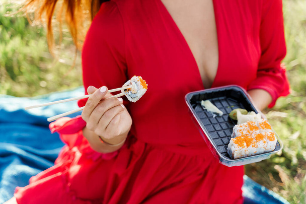 Closeup sushi nastavit dodávku jídla. Sexy dívka drží sushi s hůlkami v rukou. Kurýr doručil sushi set pro hezkou ženu. Černá krabice se sushi, wasabi, zázvorem. - Fotografie, Obrázek