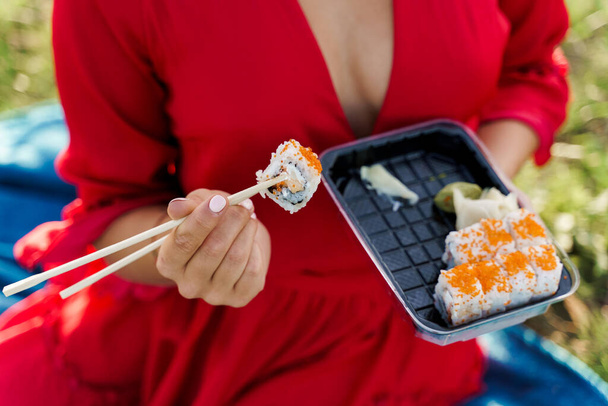 Nahaufnahme Sushi-Set Essenslieferung. Sexy girl hält Sushi mit Essstäbchen in der Hand. Kurier lieferte Sushi-Set für hübsche Frau. Black Box mit Sushi, Wasabi, Ingwer. - Foto, Bild