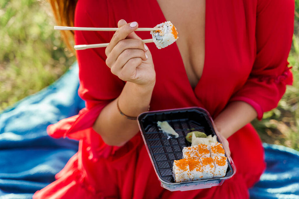 Detailní záběr sushi nastavit dodání jídla. Sexy dívka drží sushi s hůlkami v rukou. Kurýr doručil sushi set pro hezkou ženu. Černá krabice se sushi, wasabi, zázvorem. - Fotografie, Obrázek