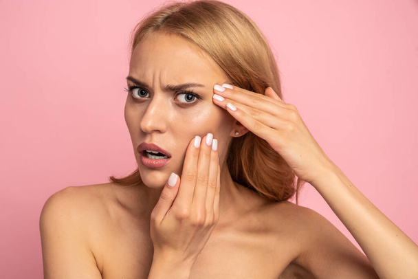 Upset, nude, natural girl touching cheek with fingers having dry oiled skin, minerals, vitamins, detox, moisturizing, hydration concept isolated on pink background. - Photo, Image