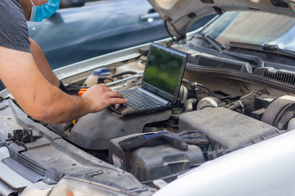auto mechanic with protective mask diagnosing car with black laptop - Photo, Image